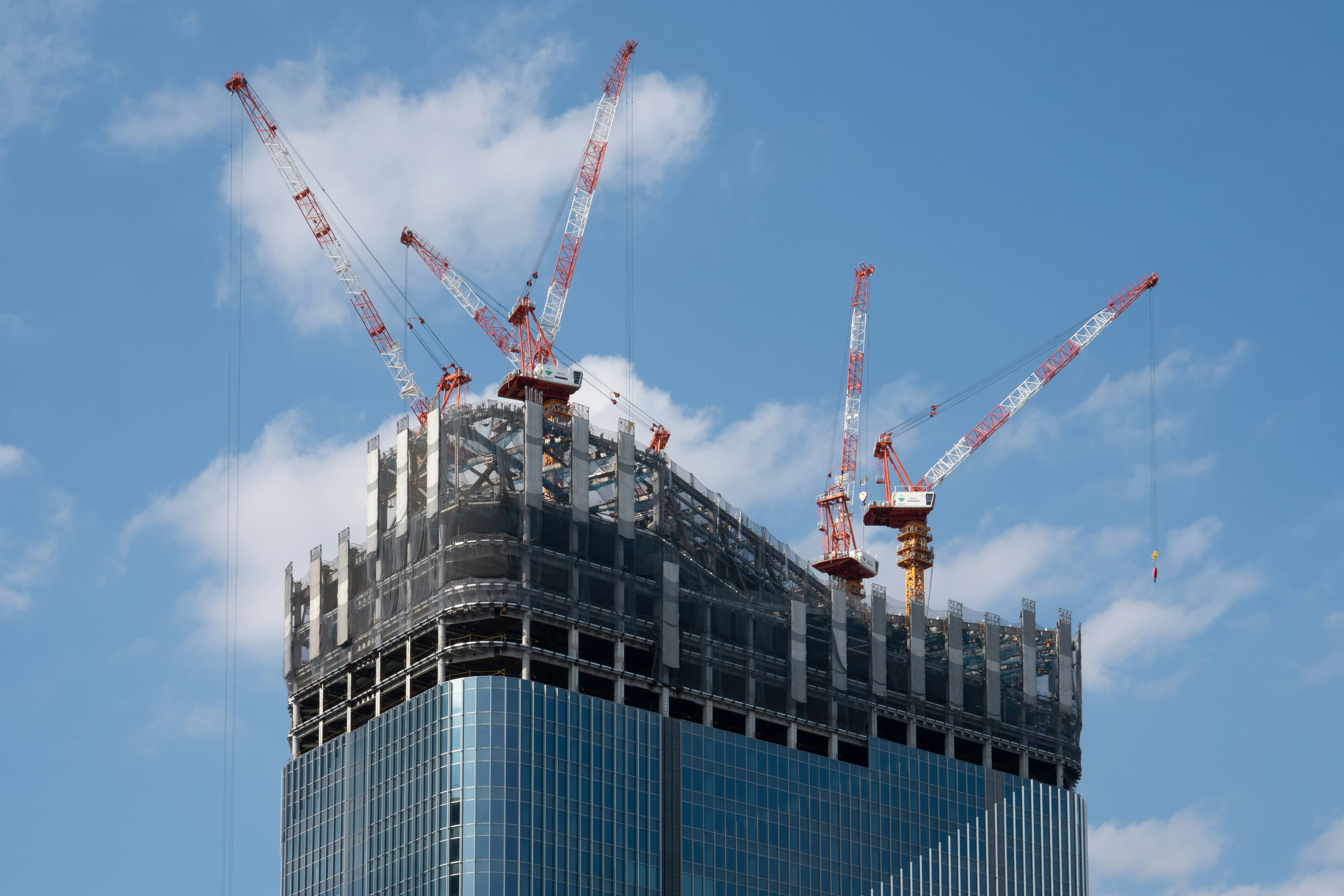 Modern skyscraper under construction with cranes against blue sky